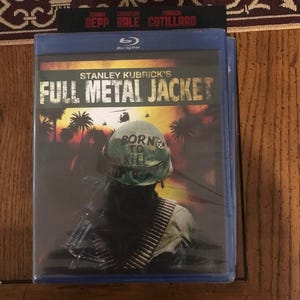 May include: A Blu-ray disc case for Stanley Kubrick's film "Full Metal Jacket." The cover art shows a soldier in a helmet with the words "Born to Kill" and a machine gun. The case is blue with the Blu-ray logo.