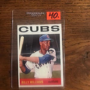 May include: A baseball card featuring Billy Williams of the Chicago Cubs. The card shows Williams in his Cubs uniform, holding a bat. The word "CUBS" is printed at the top, with "BILLY WILLIAMS" and "outfield" at the bottom. A red price tag with the number 40 is in the upper right corner.