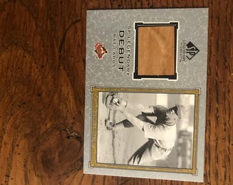 May include: A baseball card featuring a black and white image of a baseball player in action. The card has a wooden inlay and text that reads "SP Legendary Debut Bat Cards". The card is set against a gray background.