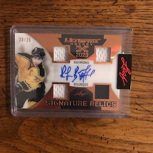 May include: A hockey card featuring Raymond Bourque, a professional ice hockey player. The card is a Signature Relics card from the 2023 Ultimate Hockey series. The card is numbered 20/25. The card features a photo of Bourque in his hockey uniform, along with his autograph and a piece of his jersey.