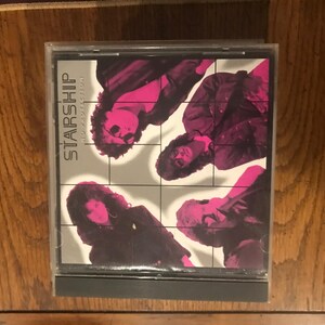 May include: A CD case featuring the album cover for Starship's 'Love Among the Cannibals'. The cover art shows four band members in a grid pattern, with a pink and black color scheme. The band's name is prominently displayed.