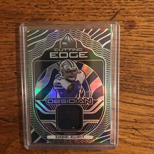 Peut inclure: Une carte de collection de football représentant Ezekiel Elliott des Cowboys de Dallas. La carte est intitulée "Cutting Edge Obsidian" et est enfermée dans une pochette de protection en plastique. La carte a un morceau de maillot noir.