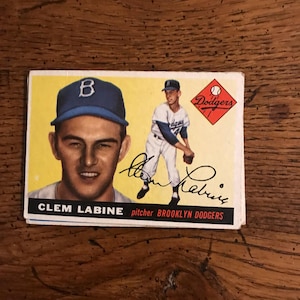 May include: Vintage baseball card featuring Clem Labine, pitcher for the Brooklyn Dodgers. The card has a yellow background with a portrait of Labine and an action shot. The Dodgers logo is visible.