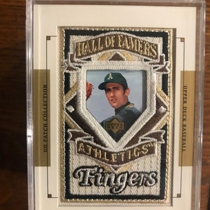 Può includere: Una carta di baseball con una foto di Rollie Fingers, un giocatore di baseball della Hall of Fame. La carta è della collezione Upper Deck Baseball e presenta una toppa con il nome di Fingers e il logo della squadra.