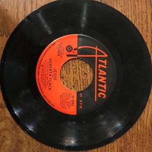 May include: A black vinyl record with an orange label. The label has the text "ATLANTIC" in a white font and the text "JESSE ROBERTA FLACK" in a white font. The record is a 45 RPM record and the catalog number is 45-2982.