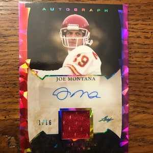 Puede incluir: Una tarjeta de deporte roja, blanca y azul con una foto de Joe Montana, un jugador de fútbol americano, vistiendo una camiseta roja y blanca. La tarjeta está numerada 1/16 y tiene un parche de camiseta roja. La tarjeta tiene el texto "AUTOGRAPH" y "JOE MONTANA" y una firma.