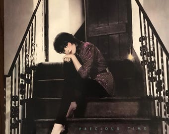May include: A black and white album cover with the text "PAT BENATAR" in large white letters at the top. A woman with dark hair is sitting on a staircase. The text "PRECIOUS TIME" is at the bottom of the image.