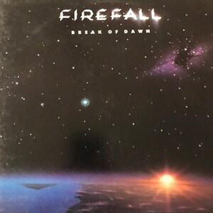May include: Album cover for Firefall's "Break of Dawn." The artwork depicts a night sky filled with stars, a sunrise over a body of water, and the band's name in white, stylized font.