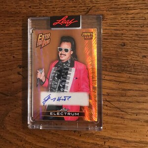 May include: A trading card featuring Jimmy Hart in a pink blazer and sunglasses, holding a microphone. The card is encased in a clear protective holder. The card has the text "ENTER THE RING", "JIMMY HART", and "LEAF ELECTRUM".