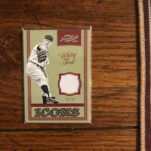 May include: A baseball trading card featuring Whitey Ford in a pitching pose. The card has a cream background with red and gold accents, and the word "ICONS" is printed at the bottom. The card is encased in a protective sleeve.