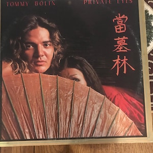 Könnte beinhalten: Ein Vinyl-Plattencover mit einem Mann und einer Frau, vor denen sich ein roter und goldener Fächer befindet. Das Album trägt den Titel "Private Eyes" und der Künstler ist "Tommy Bolin". Das Plattencover zeigt auch japanische Schriftzeichen.