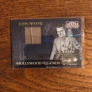 May include: A trading card featuring John Wayne, an American actor. The card is blue and silver with a picture of John Wayne in a suit. The card has the text "Donruss Americana" and "Hollywood Legends" on it.