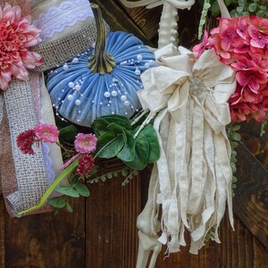 May include: A blue velvet pumpkin with white pearl accents, a pink flower with a burlap bow, a white fabric bow with a beaded embellishment, and a pink hydrangea with green leaves.