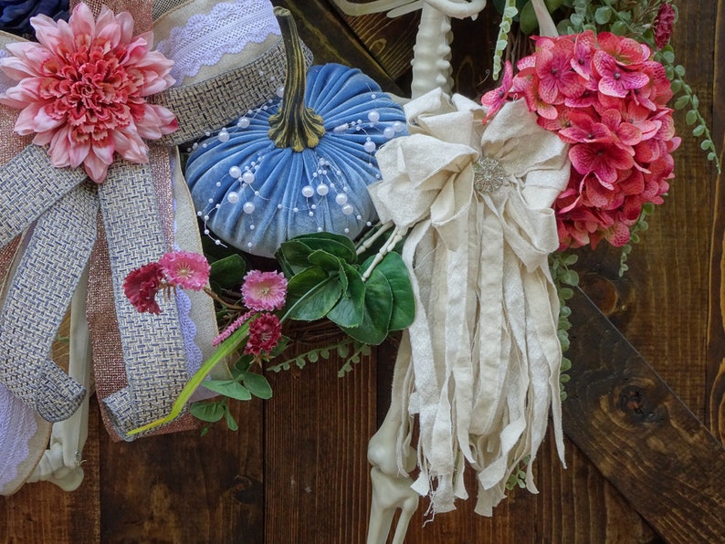 May include: A blue velvet pumpkin with white pearl accents, a pink flower with a burlap bow, a white fabric bow with a beaded embellishment, and a pink hydrangea with green leaves.