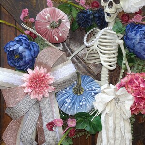May include: A fall wreath with a skeleton, blue, pink, and white velvet pumpkins, and a variety of flowers in shades of pink, blue, and white.