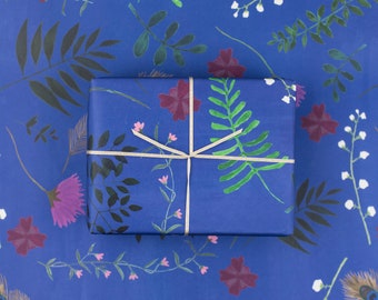 Può includere: Carta da regalo blu con un motivo floreale con fiori rosa e viola, foglie verdi e fiori bianchi. La carta da regalo è legata con un nastro beige.