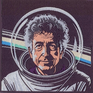 May include: A square embroidered patch featuring a portrait of a person with curly hair wearing a space suit with a circular helmet visor. The background includes horizontal stripes in blue, green, and white against a dark purple fabric base.