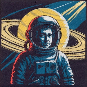 May include: A square embroidered patch featuring an astronaut in a white helmet with a blue-tinted visor. The astronaut is centered against a large yellow planet with prominent rings. The background is dark blue with light blue streaks of light.