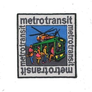 May include: A white and gray embroidered patch with the text "metrotransit" repeated four times around the border. The center of the patch features a green and yellow bus with people getting on. A helicopter is flying above the bus.