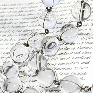 May include: A vintage glass bead necklace with clear glass beads and a silver wire. The beads are strung on a silver chain and the necklace is lying on a page of a book.