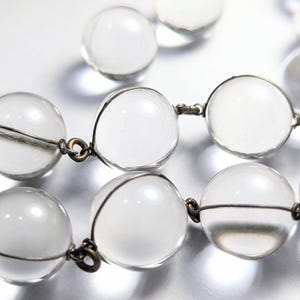 May include: A clear crystal beaded necklace with silver wire connecting the beads. The beads are round and have a smooth, polished finish.
