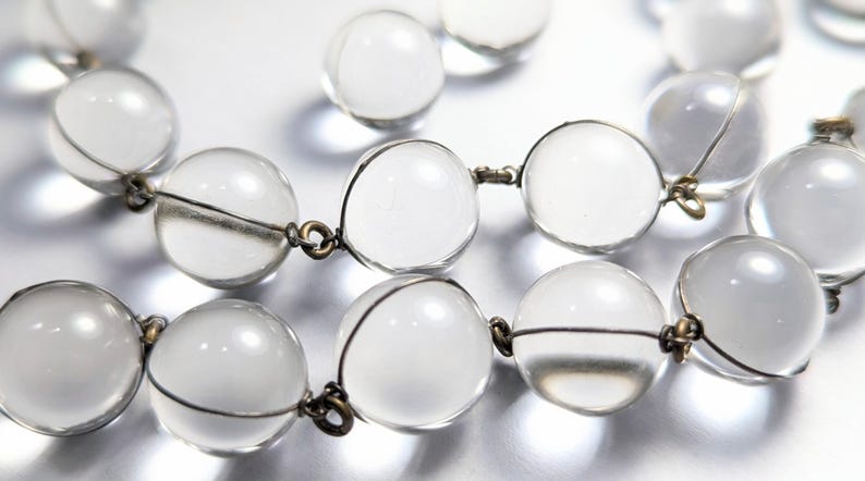 May include: A clear crystal beaded necklace with silver wire connecting the beads. The beads are round and have a smooth, polished finish.