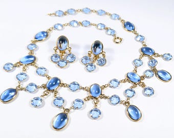 May include: A vintage jewelry set featuring a necklace, bracelet, and earrings. The set has a gold-tone metal setting with oval and round light blue stones. The earrings have a cluster design, and the necklace and bracelet have a linked design.