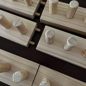 May include: Four wooden wall mounted coat racks with dowel pegs. The racks are made of unfinished pine wood and have a natural wood finish. Each rack has a different number of pegs.