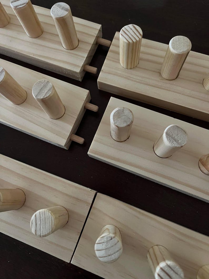 May include: Four wooden wall mounted coat racks with dowel pegs. The racks are made of unfinished pine wood and have a natural wood finish. Each rack has a different number of pegs.