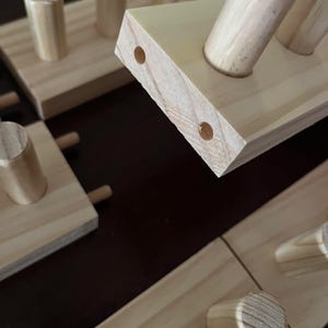 May include: Close-up of a wooden shelf with multiple dowel pegs. The shelf is made of natural wood with a light brown finish. The dowel pegs are also made of natural wood and are arranged in a staggered pattern.