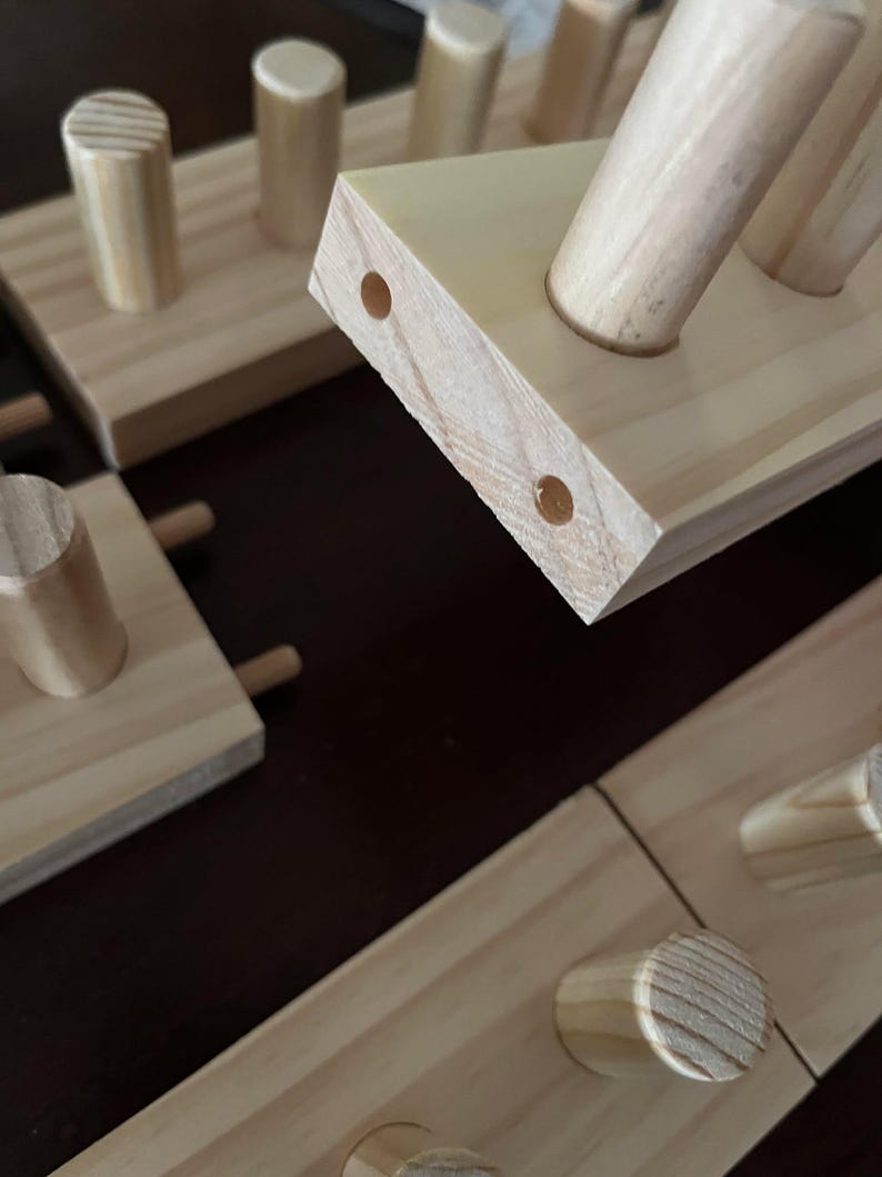 May include: Close-up of a wooden shelf with multiple dowel pegs. The shelf is made of natural wood with a light brown finish. The dowel pegs are also made of natural wood and are arranged in a staggered pattern.