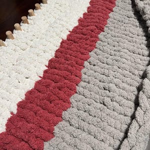 May include: A chunky knit throw blanket with stripes of white, red, and gray yarn.