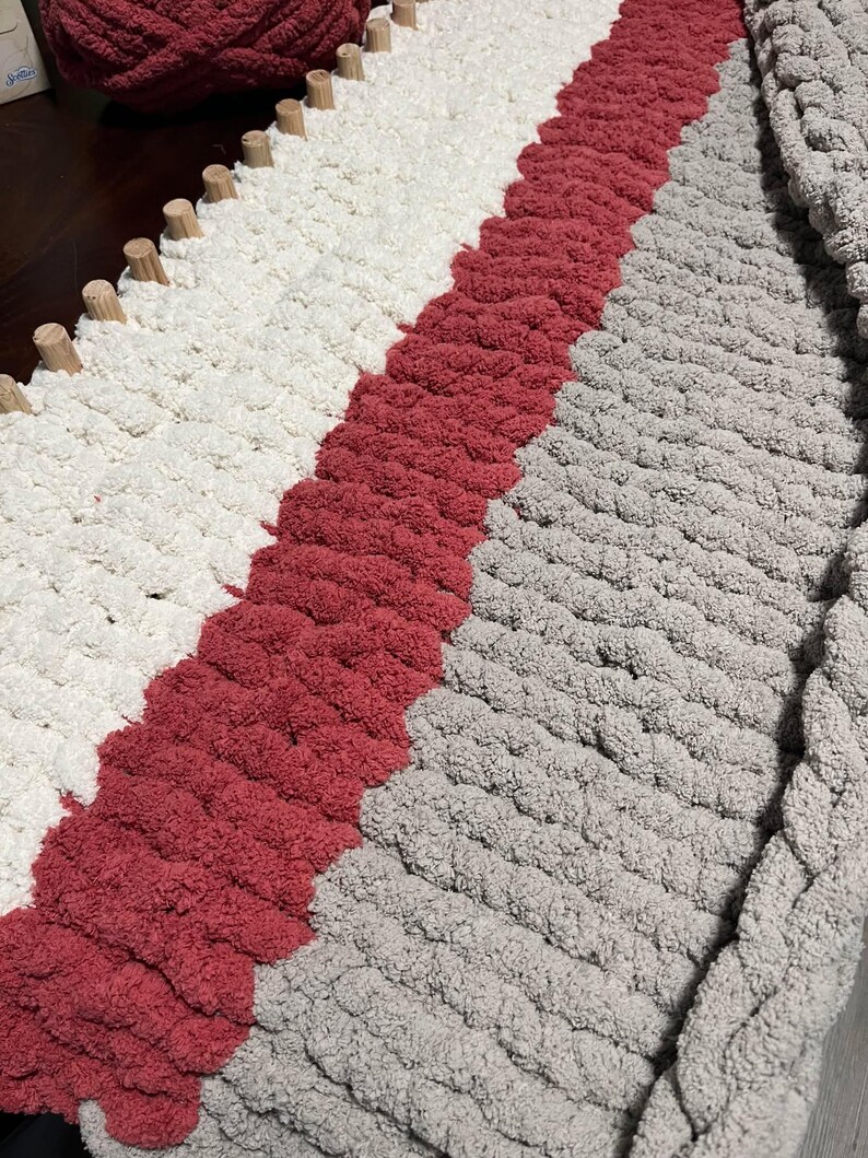 May include: A chunky knit throw blanket with stripes of white, red, and gray yarn.