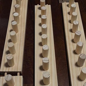 May include: A set of three wooden wall organizers with rows of dowels for hanging items. Each organizer has a light wood finish and is mounted on a wall.