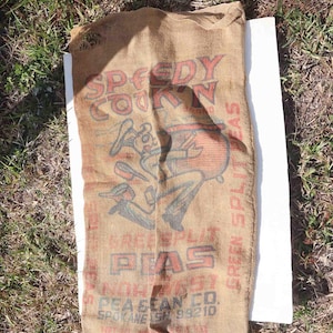 May include: Vintage burlap sack with red and blue graphics. The sack features the text "Speedy Corn" and an illustration of a rabbit. The words "Green Split Peas" and "Pea Bean Co. Spokane WA 99210" are also visible.