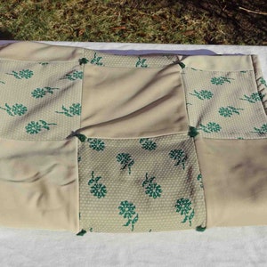May include: A beige patchwork clutch with a floral pattern in green. The clutch is rectangular and appears to be made of fabric. The patches are sewn together with green thread.