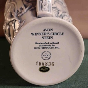 Puede incluir: Una jarra de cer&aacute;mica blanca con el texto "AVON WINNER'S CIRCLE STEIN" y "Handcrafted in Brazil". La base de la jarra tiene el n&uacute;mero "154836" y el logotipo de Avon. La jarra es un art&iacute;culo de colecci&oacute;n.