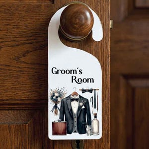 May include: A white door hanger with the text Groom's Room in black lettering. The design features a black tuxedo jacket, a grey vest, a white shirt, a bowtie, a boutonniere, a brown flask, a glass, and a floral bouquet illustration.
