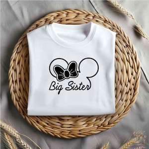 May include: White t-shirt with a black silhouette of Mickey Mouse ears with a bow on top. The text "Big Sister" is printed below the ears.