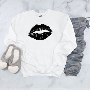 May include: White sweatshirt with a black lips graphic print. The sweatshirt is a casual, comfortable style.