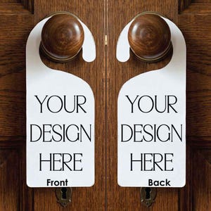 May include: Two white door hangers with a rounded top cutout, each featuring the black printed text 'YOUR DESIGN HERE'. One hanger is labeled 'Front' at the bottom, and the other is labeled 'Back' at the bottom, both hanging on wooden knobs.