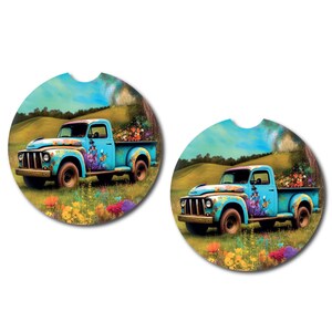 May include: Two round blue and white car coasters with a vintage blue pickup truck with flowers in the bed driving through a field of flowers. The truck is painted with flowers and butterflies.