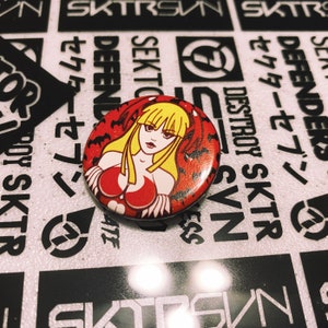 May include: A red and black button featuring a cartoon woman with blonde hair and a red outfit. The woman is surrounded by bats. The button has a white background.