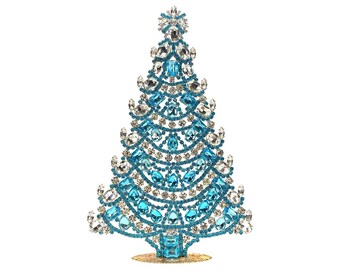 May include: A decorative Christmas tree sculpture. The tree is made of blue and clear crystals, arranged in a festive design. The base is gold-colored. The tree is a sparkling holiday decoration.