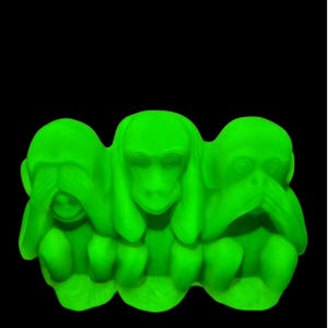 May include: A neon green sculpture of the three wise monkeys: see no evil, hear no evil, speak no evil. The monkeys are depicted in a seated position with their hands covering their eyes, ears, and mouth. The background is black.