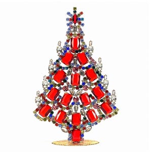 May include: A decorative tree ornament constructed from a metal frame encrusted with numerous faceted red rectangular crystals, interspersed with smaller clear, blue, green, and pink rhinestones, all supported by a circular gold-toned base.