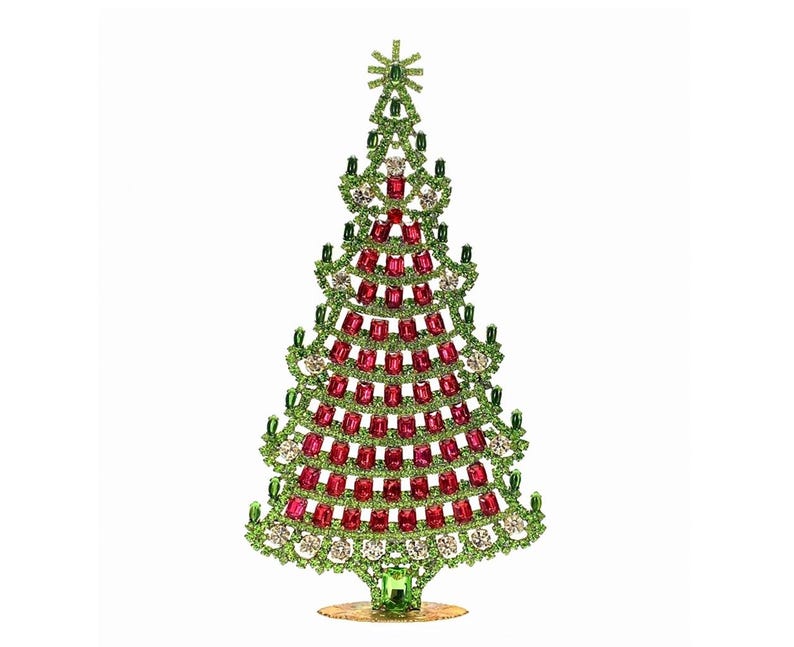 Op de afbeelding: Een decoratief kerstboomfiguur. De boom is versierd met groene, rode en heldere kristallen. De boom heeft een ster op de top en staat op een goudkleurige basis. Een feestelijke vakantiedecoratie.