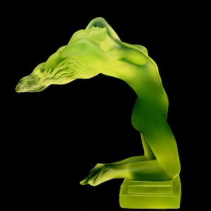 May include: A green glass sculpture of a woman with her head thrown back and her hair flowing. The sculpture is on a square base.
