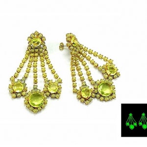 May include: A pair of gold tone chandelier earrings with multiple strands of rhinestones and large green stones. The earrings glow green in the dark.