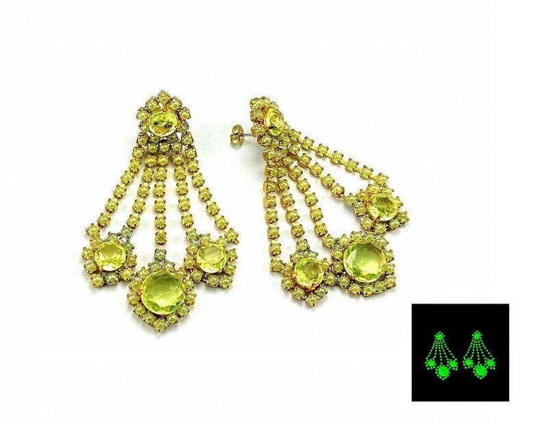 May include: A pair of gold tone chandelier earrings with multiple strands of rhinestones and large green stones. The earrings glow green in the dark.